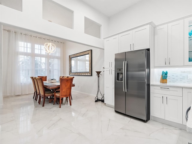 kitchen with stainless steel refrigerator with ice dispenser, white cabinetry, tasteful backsplash, decorative light fixtures, and a high ceiling