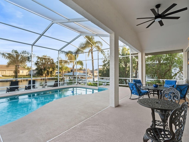 view of pool with a patio area, a water view, ceiling fan, and glass enclosure