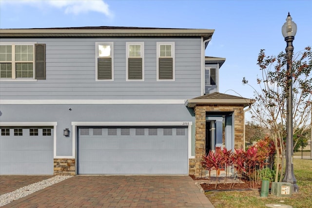 view of front of property featuring decorative driveway, stone siding, a garage, and stucco siding