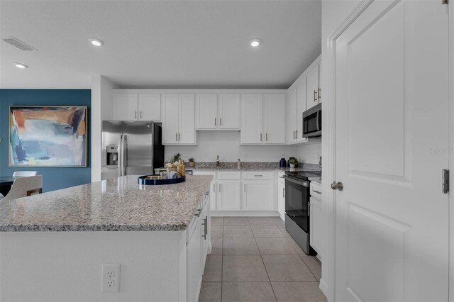 kitchen with light tile patterned floors, a center island, white cabinets, and appliances with stainless steel finishes