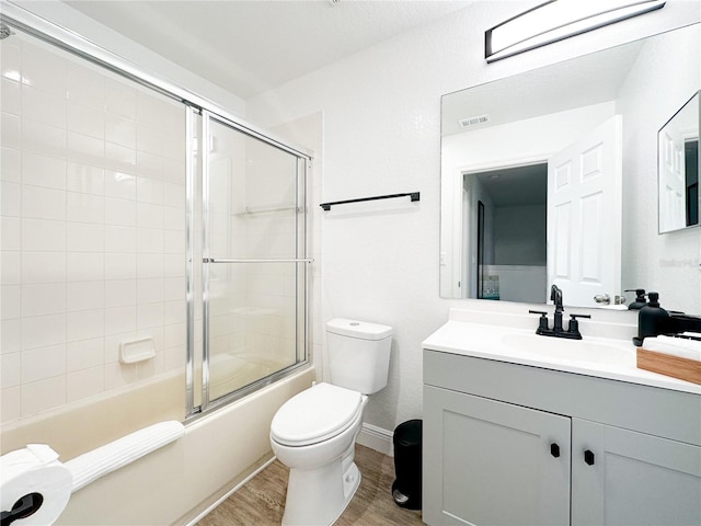 full bathroom with bath / shower combo with glass door, vanity, wood-type flooring, and toilet