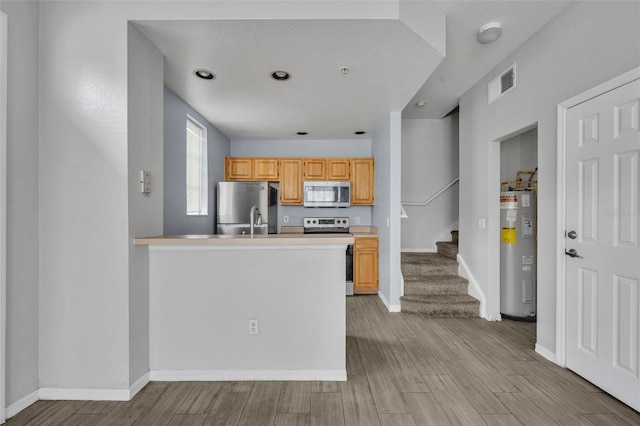 kitchen featuring appliances with stainless steel finishes, electric water heater, light brown cabinetry, and kitchen peninsula