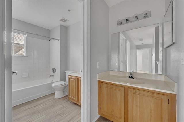 full bathroom with hardwood / wood-style floors, vanity, tiled shower / bath, and toilet