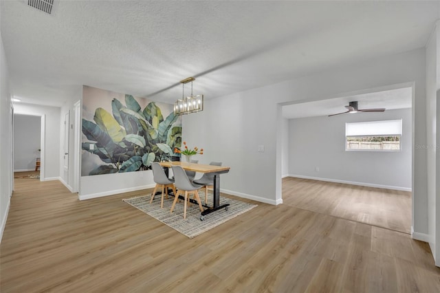 dining space with ceiling fan with notable chandelier, light hardwood / wood-style flooring, and a textured ceiling