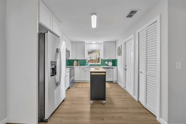 kitchen with white cabinetry, a center island, stainless steel appliances, light hardwood / wood-style floors, and backsplash