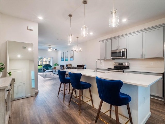 kitchen featuring gray cabinets, sink, hanging light fixtures, stainless steel appliances, and a center island with sink