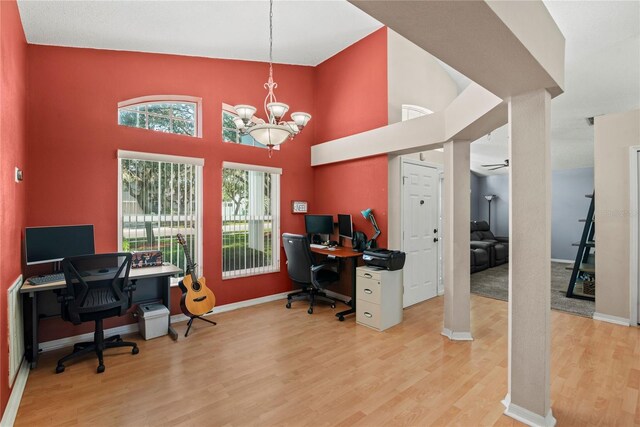 home office with a towering ceiling, a chandelier, and light wood-type flooring