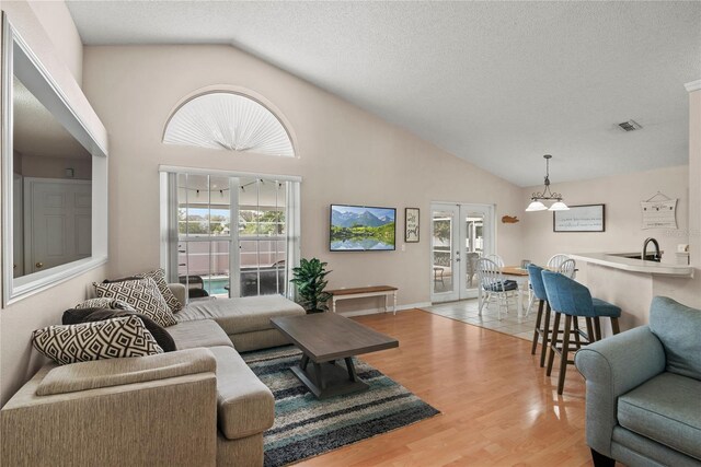 living room with french doors, high vaulted ceiling, a textured ceiling, and light wood-type flooring