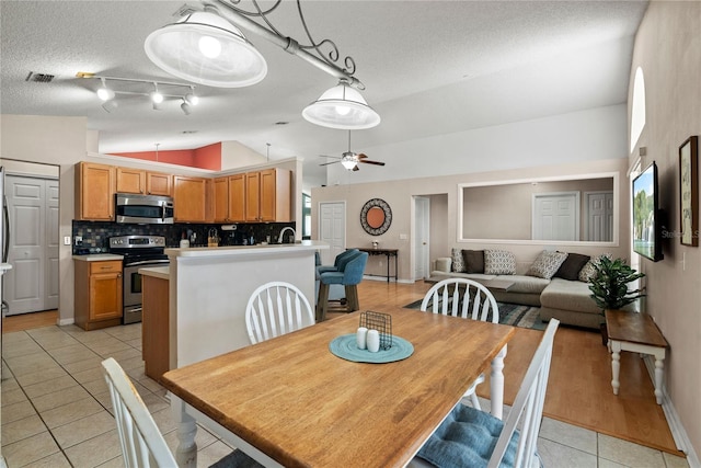 dining room featuring light tile patterned flooring, lofted ceiling, ceiling fan, and a textured ceiling