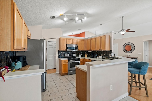 kitchen with lofted ceiling, a breakfast bar, light tile patterned floors, appliances with stainless steel finishes, and kitchen peninsula