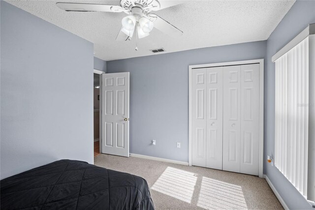 carpeted bedroom featuring ceiling fan, a closet, and a textured ceiling