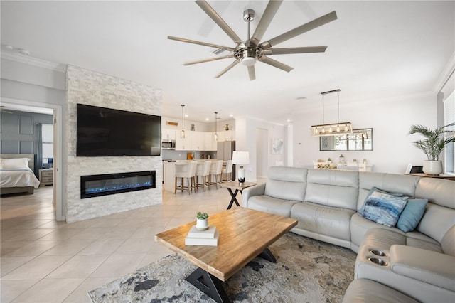 living room featuring ceiling fan, ornamental molding, a fireplace, and light tile patterned floors