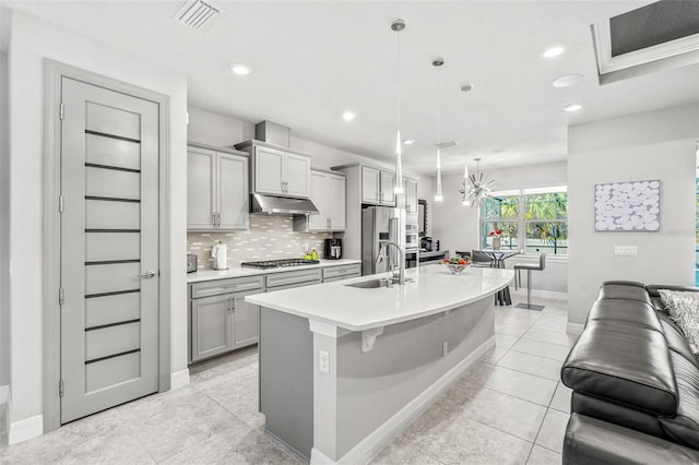 kitchen featuring a center island with sink, sink, gray cabinetry, and pendant lighting