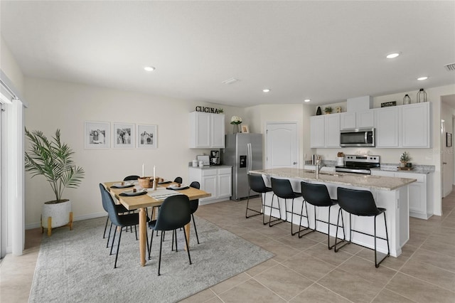 kitchen featuring white cabinetry, stainless steel appliances, a kitchen breakfast bar, light stone countertops, and a center island with sink