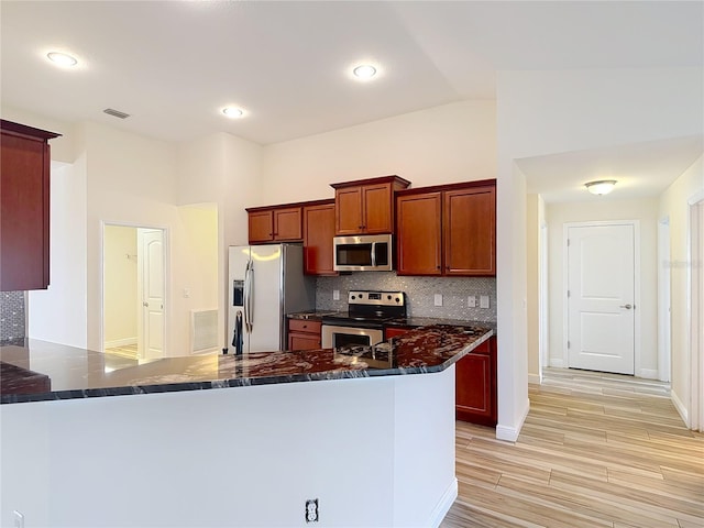 kitchen with lofted ceiling, dark stone countertops, backsplash, stainless steel appliances, and kitchen peninsula