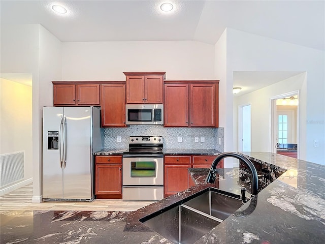 kitchen featuring lofted ceiling, sink, tasteful backsplash, dark stone countertops, and stainless steel appliances