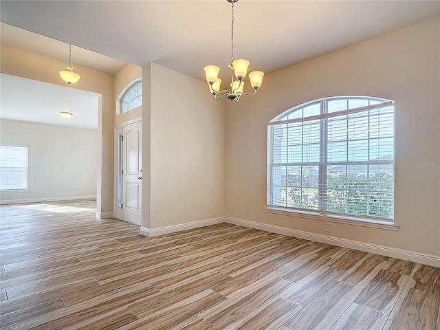 unfurnished room featuring a notable chandelier and light wood-type flooring