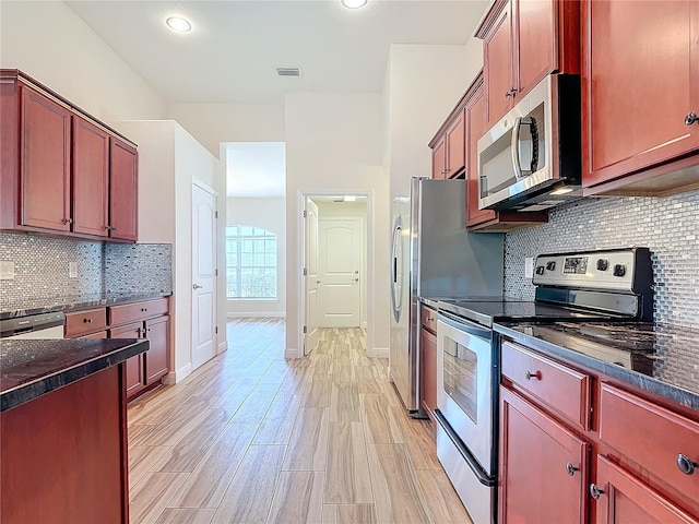 kitchen with stainless steel appliances, dark stone counters, and backsplash