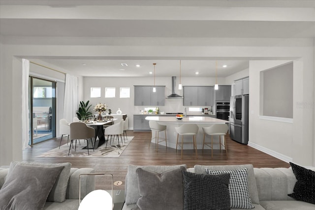 kitchen with wall chimney range hood, a breakfast bar, appliances with stainless steel finishes, hanging light fixtures, and a center island