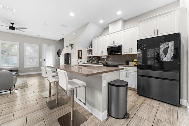 kitchen featuring black refrigerator, white cabinetry, backsplash, a kitchen breakfast bar, and a center island with sink