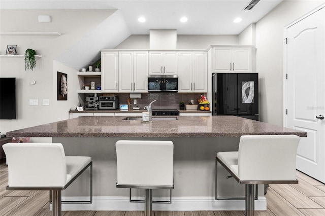 kitchen featuring sink, black fridge, a center island with sink, a kitchen breakfast bar, and white cabinets