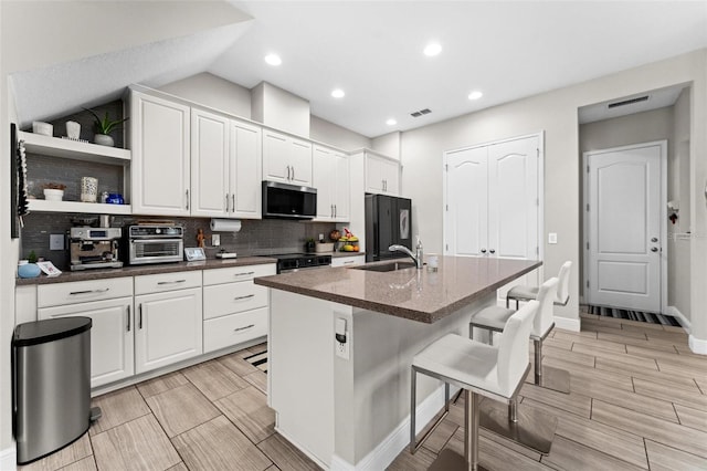 kitchen featuring a kitchen bar, refrigerator, a center island with sink, and white cabinets