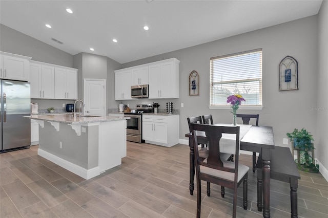 kitchen featuring light stone countertops, appliances with stainless steel finishes, a center island with sink, and white cabinets