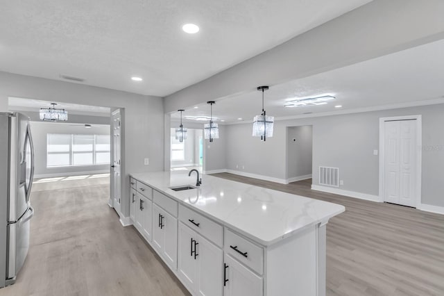 kitchen with sink, white cabinetry, light stone counters, hanging light fixtures, and stainless steel fridge