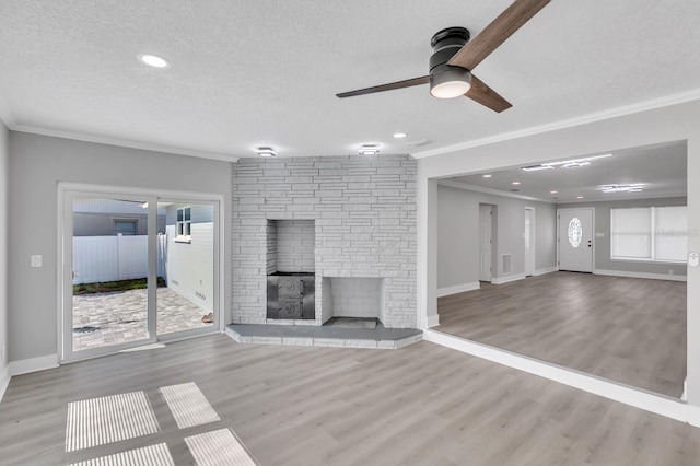 unfurnished living room featuring crown molding, light wood-type flooring, a textured ceiling, and a fireplace