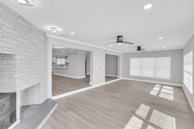 unfurnished living room with a fireplace, ceiling fan, light hardwood / wood-style floors, crown molding, and a textured ceiling