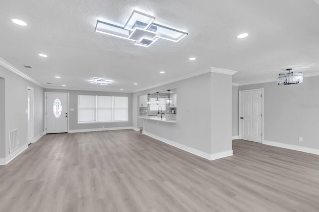 unfurnished living room featuring crown molding, sink, a textured ceiling, and light wood-type flooring