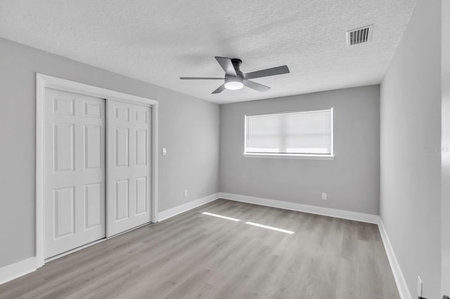 unfurnished bedroom with ceiling fan, a closet, a textured ceiling, and light wood-type flooring