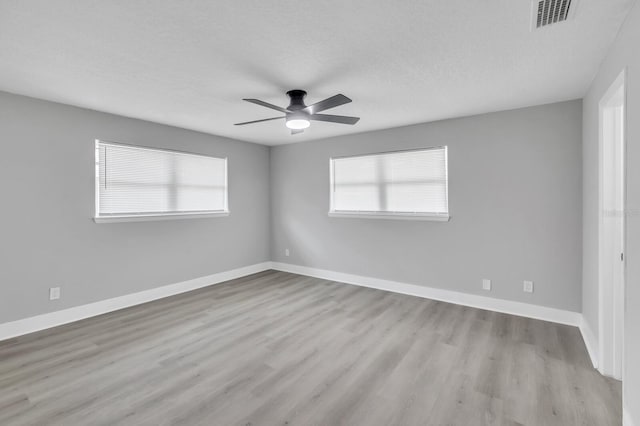 empty room featuring ceiling fan, light wood-type flooring, a textured ceiling, and a wealth of natural light