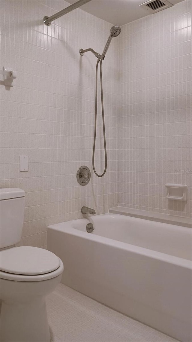 bathroom featuring tiled shower / bath combo, tile patterned flooring, tile walls, and toilet