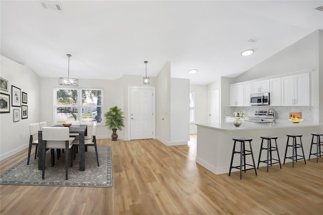 dining space with vaulted ceiling, sink, and light hardwood / wood-style floors