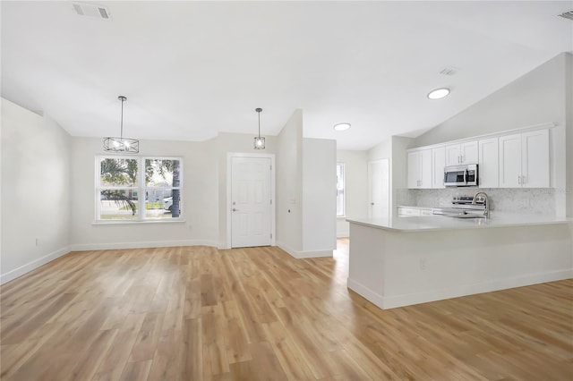 kitchen with hanging light fixtures, white cabinetry, appliances with stainless steel finishes, and vaulted ceiling