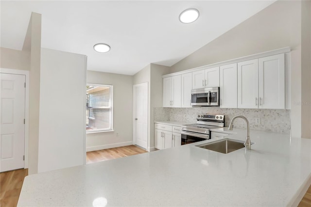 kitchen with lofted ceiling, sink, appliances with stainless steel finishes, kitchen peninsula, and white cabinets