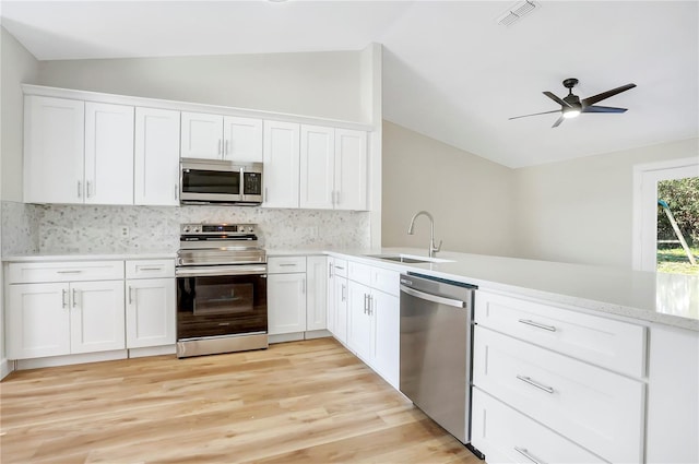 kitchen with sink, white cabinetry, stainless steel appliances, vaulted ceiling, and kitchen peninsula