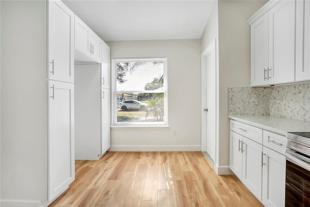 kitchen with white cabinetry, stainless steel stove, backsplash, and light hardwood / wood-style flooring