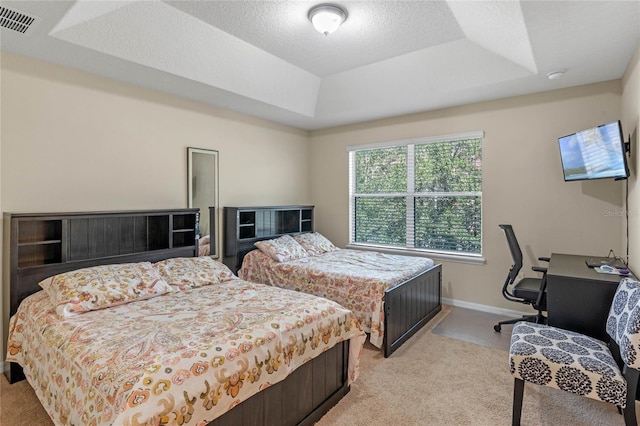 bedroom with light colored carpet, a tray ceiling, and a textured ceiling