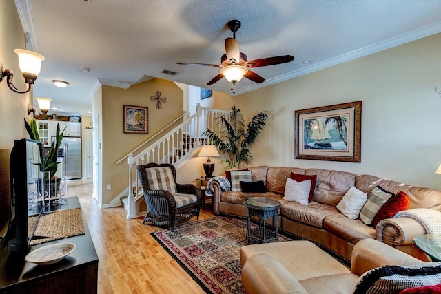 living room with ceiling fan, ornamental molding, a textured ceiling, and light wood-type flooring