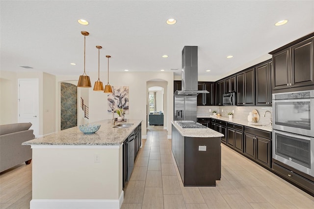 kitchen featuring sink, island range hood, hanging light fixtures, a center island with sink, and appliances with stainless steel finishes