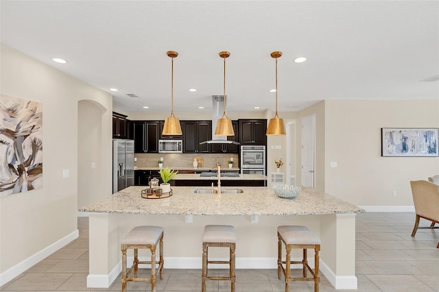 kitchen featuring appliances with stainless steel finishes, pendant lighting, an island with sink, sink, and a kitchen bar