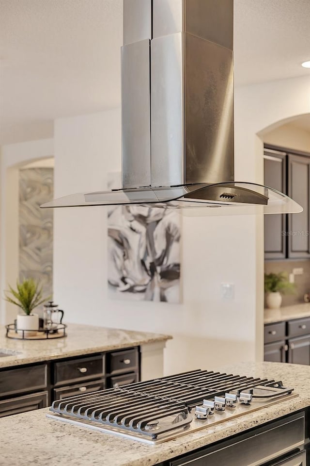 kitchen featuring light stone counters, island exhaust hood, stainless steel gas stovetop, and gray cabinetry