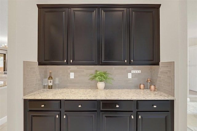 kitchen with light stone counters, dark brown cabinets, and decorative backsplash