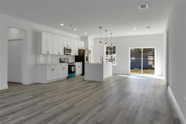 kitchen with appliances with stainless steel finishes, pendant lighting, an island with sink, white cabinets, and light wood-type flooring