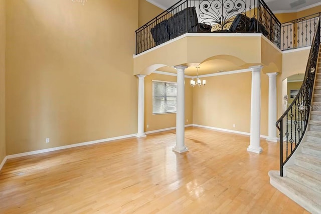 foyer with ornate columns, wood-type flooring, a towering ceiling, and crown molding