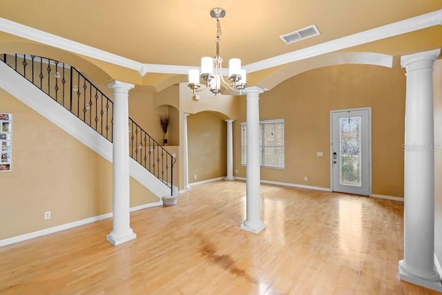 foyer entrance with crown molding, decorative columns, hardwood / wood-style floors, and a notable chandelier