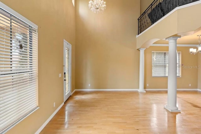 foyer with decorative columns, wood-type flooring, a towering ceiling, and a chandelier