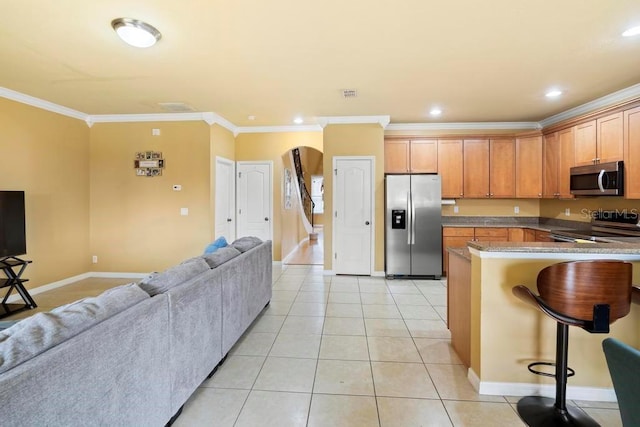 kitchen with crown molding, light tile patterned flooring, a breakfast bar, and appliances with stainless steel finishes